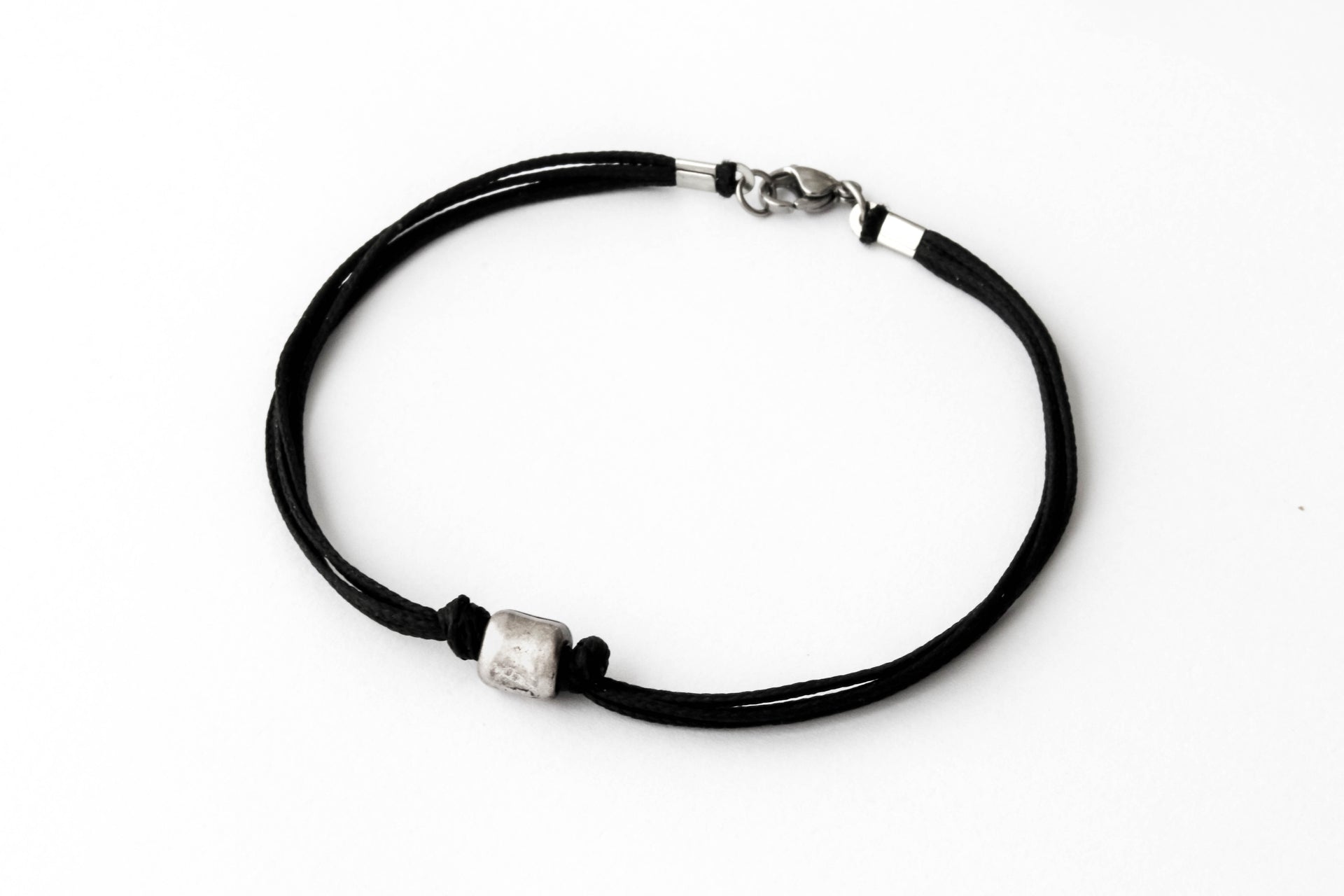 A black cord bracelet for men with a silver tube bead charm and a clasp closure.