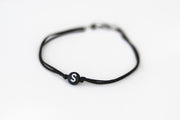 A man's wrist wearing a black cord bracelet with a black round bead and a initial letter