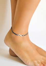 Anchored anklet with a silver infinity symbol on a foot against a neutral background