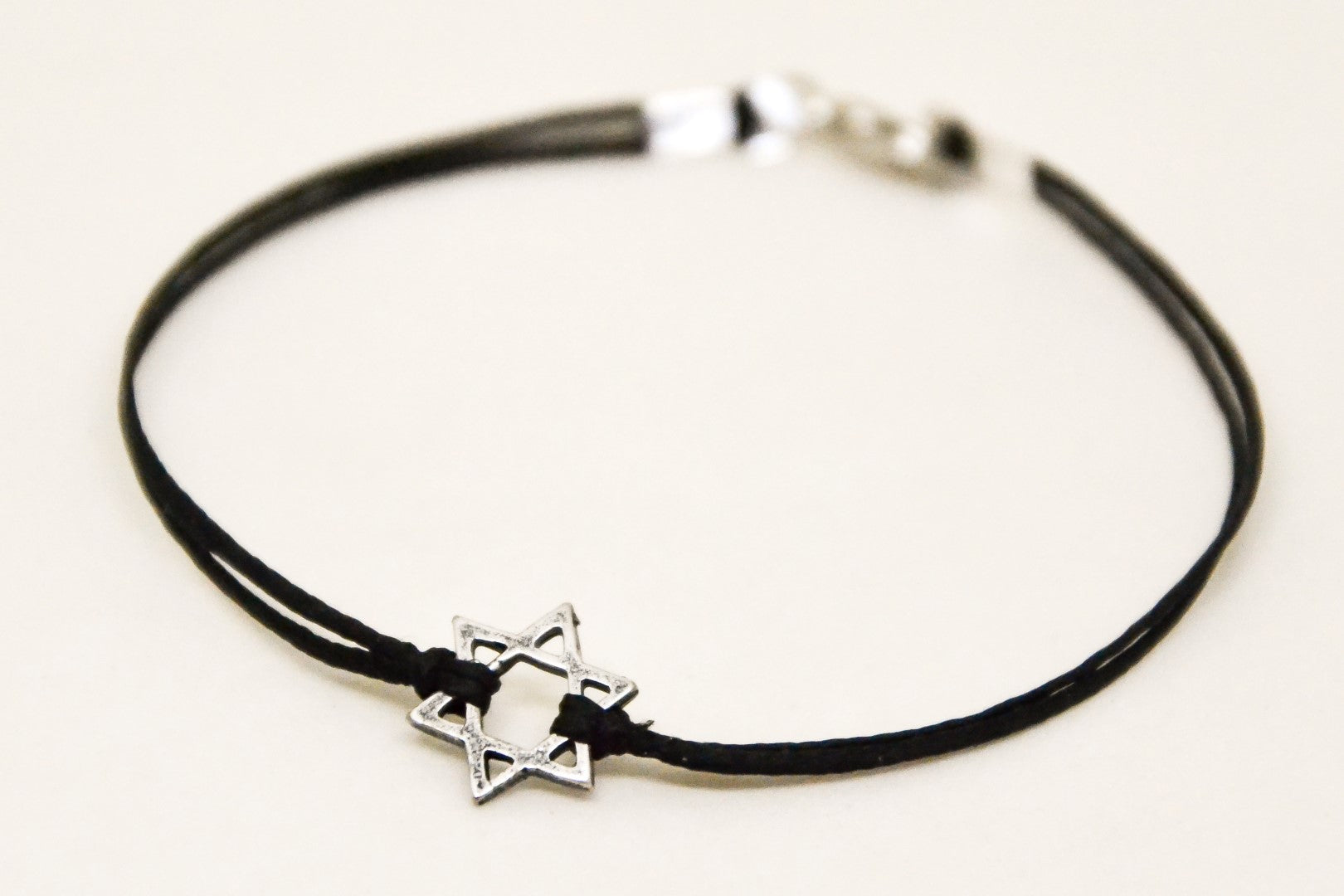 Black cord bracelet with a silver star charm on a white background