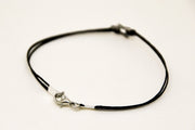 Black leather cord necklace with silver clasp on a light beige background