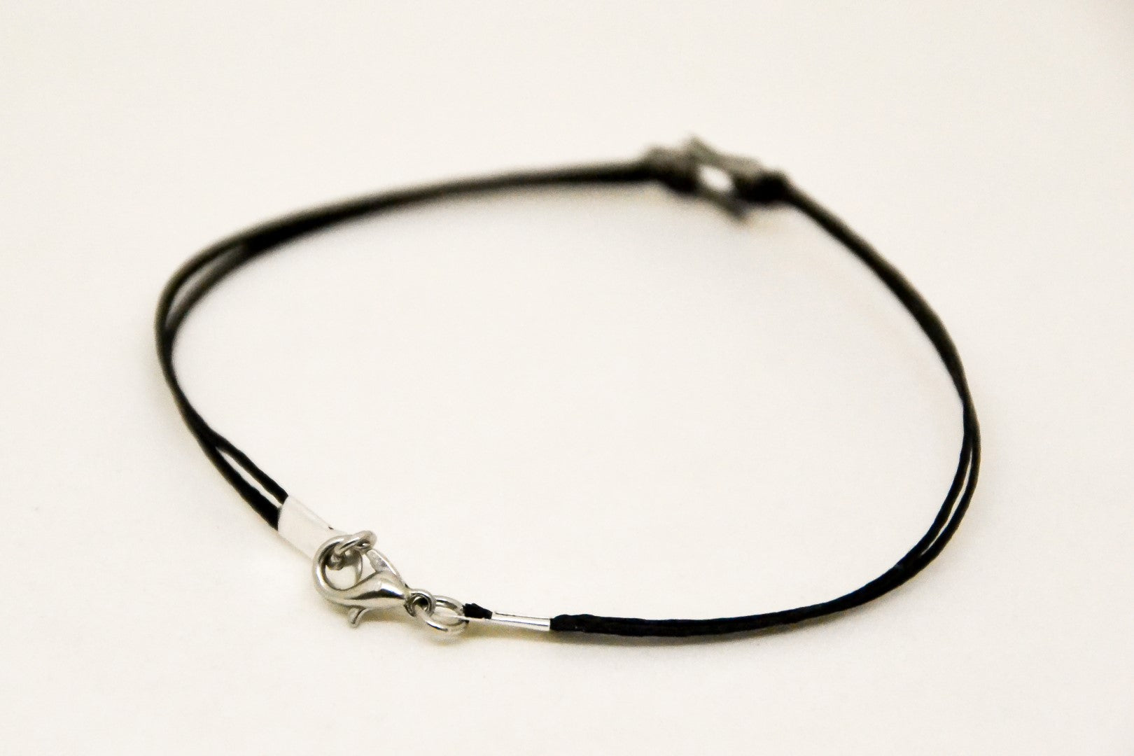 Black leather cord necklace with silver clasp on a light beige background