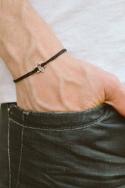 Person wearing a black bracelet with a star charm on a plain background