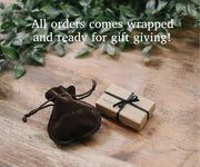 Brown velvet pouch and wrapped gift on a wooden surface with greenery in the background
