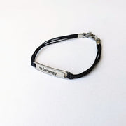 Black cord bracelet with silver tag on a white background