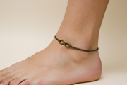 Ankle with a bronze infinity charm on a plain background