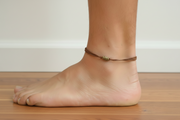 Ankle with a brown cord anklet on a wooden floor.