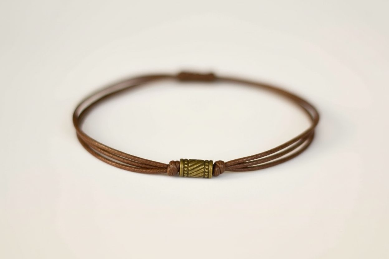 Brown leather cord bracelet with a metal clasp on a light beige background