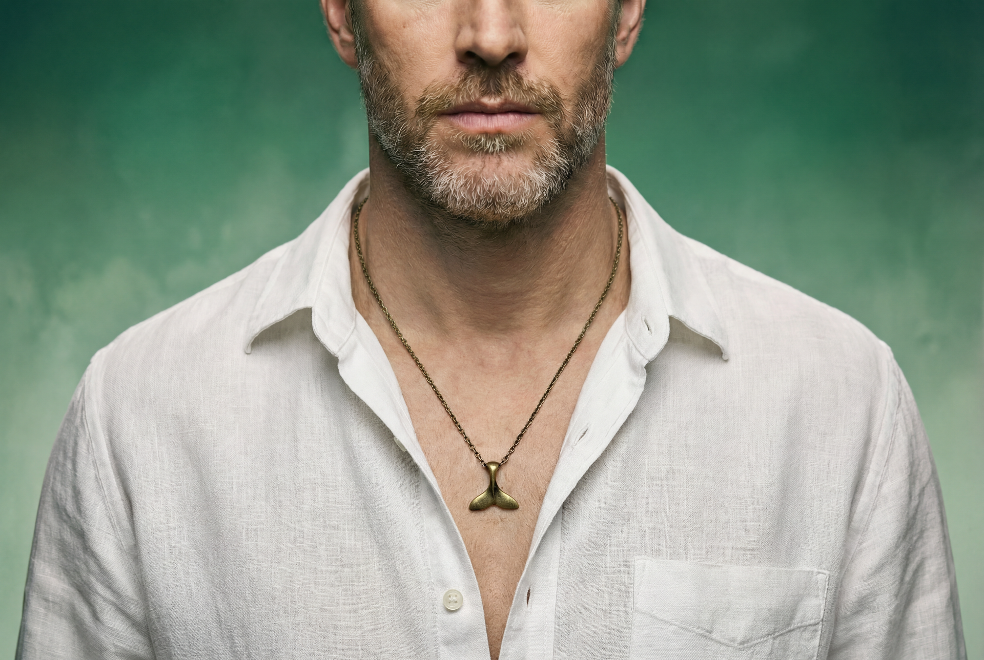 Man wearing a light-colored shirt with a bronze whale tail chain necklace against a green background