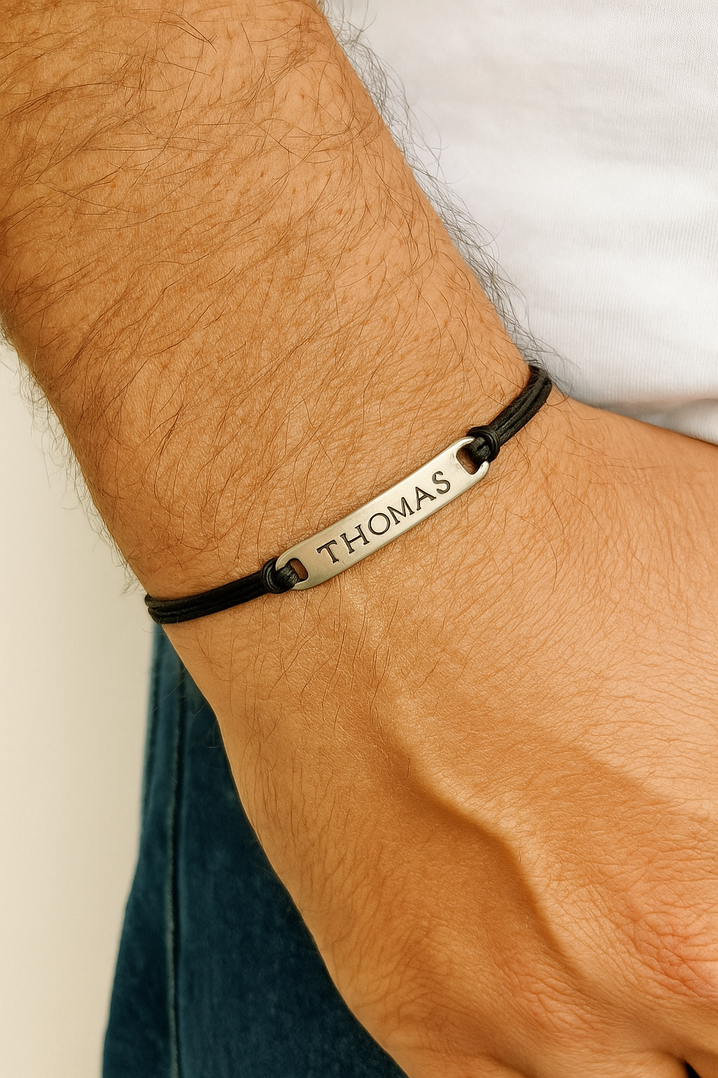 Bracelet engraved name on a wrist against a neutral background. Personalized Name Bracelet For Men Stainless Steel Charm, Silver black cotton  string cord Custom Mens Jewelry
