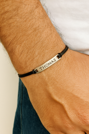 Bracelet engraved name on a wrist against a neutral background. Personalized Name Bracelet For Men Stainless Steel Charm, Silver black cotton  string cord Custom Mens Jewelry