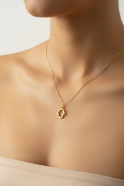 Gold necklace with a hamsa small pendant on a person's neck against a neutral background