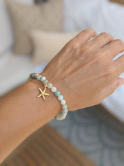 Hand wearing a bracelet with a starfish charm and amazonite beads on a blurred background
