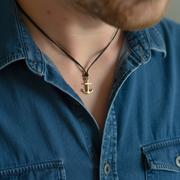 Person wearing a blue shirt with a bronze anchor pendant necklace.