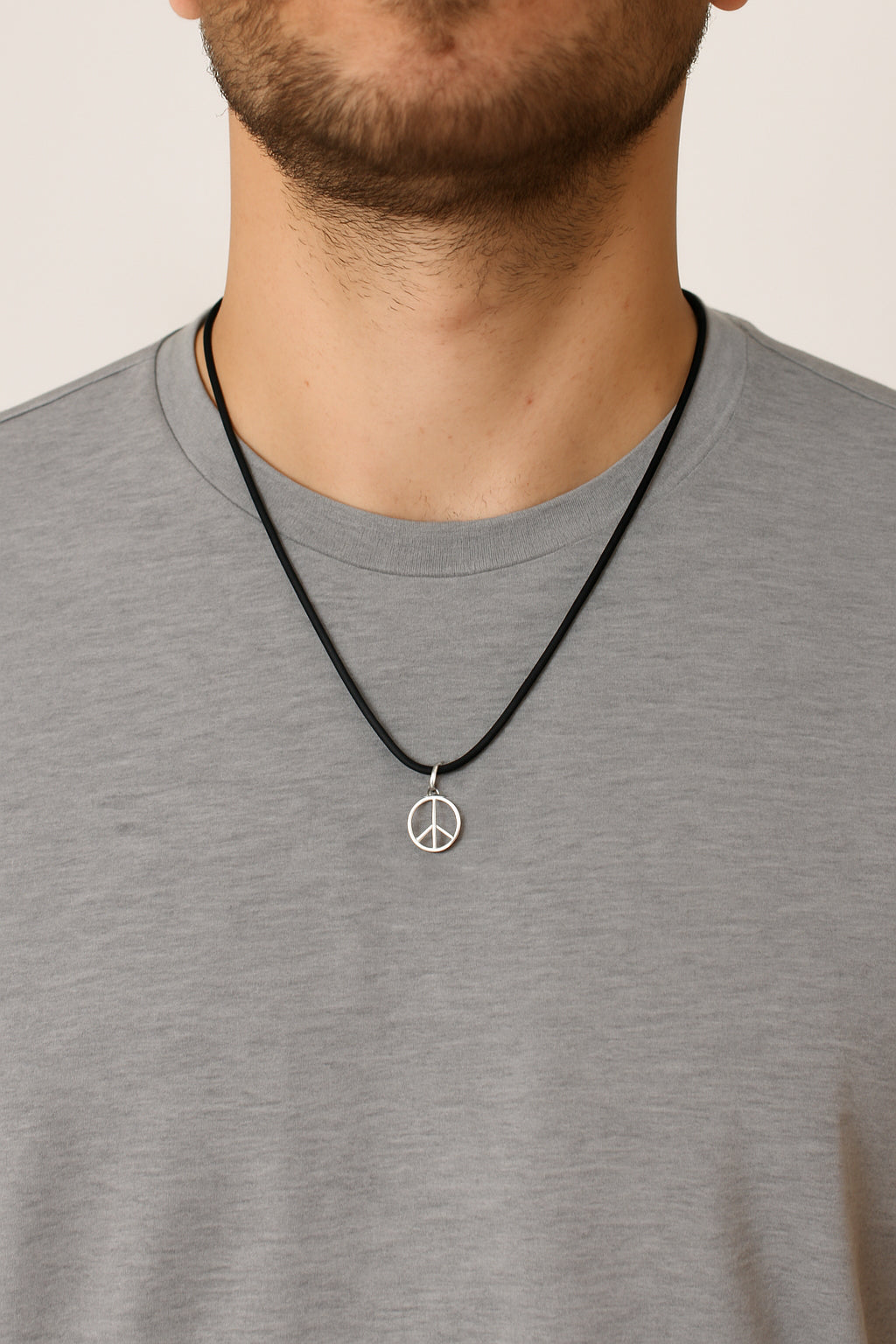 Man wearing a gray shirt with a black cord necklace featuring a peace sign pendant.