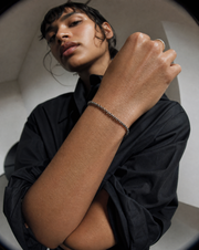 A close-up lifestyle shot of a model wearing a silver beaded chain bracelet on her wrist, paired with a gold ring on her finger and a black button-up shirt.