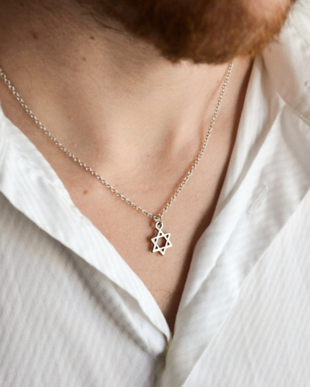 Silver necklace with a Star of David pendant worn by a person in a white shirt.