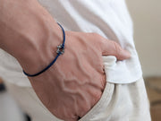 Hand wearing a blue bracelet with star charms, holding a white shirt sleeve.