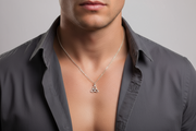 Man wearing a gray shirt with an open collar, displaying a silver necklace with a triangular trinity pendant.
