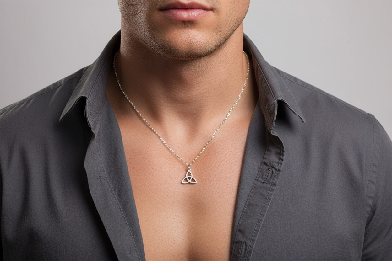 Man wearing a gray shirt with an open collar, displaying a silver necklace with a triangular trinity pendant.